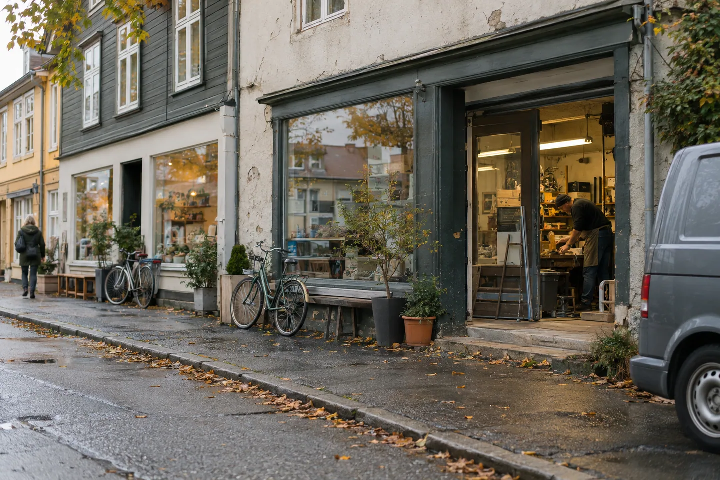 En gate med små butikker, et verksted og en servicebil i et tenkt norsk nabolag.